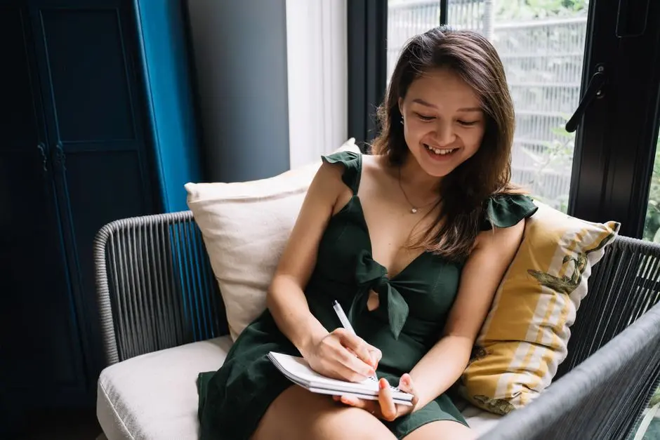 Seorang perempuan muda menulis di buku catatan sambil tersenyum
